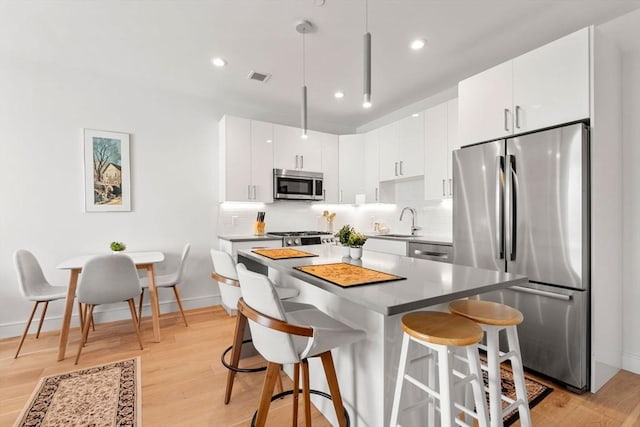 kitchen featuring sink, appliances with stainless steel finishes, hanging light fixtures, a kitchen breakfast bar, and white cabinets