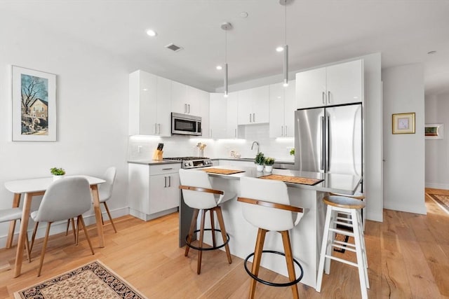 kitchen with hanging light fixtures, appliances with stainless steel finishes, white cabinets, and light wood-type flooring