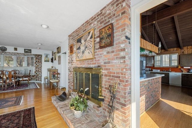 living room with beamed ceiling, sink, light hardwood / wood-style floors, and a brick fireplace