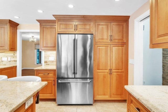 kitchen with recessed lighting, light stone counters, backsplash, and freestanding refrigerator