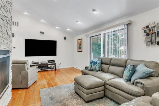 living room with visible vents, vaulted ceiling, a stone fireplace, wood finished floors, and baseboards