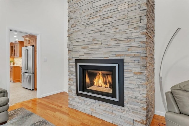 interior details featuring tasteful backsplash, freestanding refrigerator, a stone fireplace, and wood finished floors