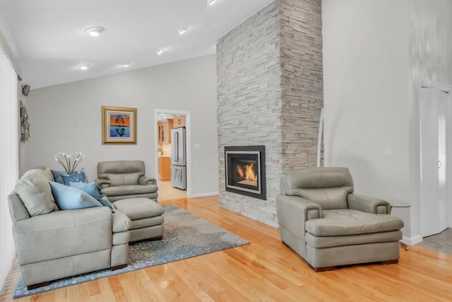 living room featuring vaulted ceiling, a fireplace, baseboards, and wood finished floors