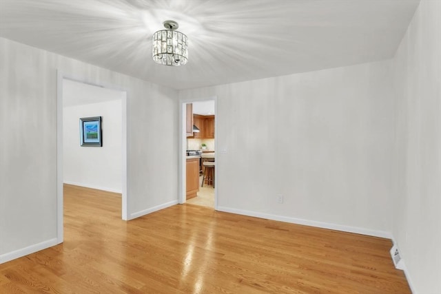 spare room with light wood-style flooring, baseboards, and an inviting chandelier