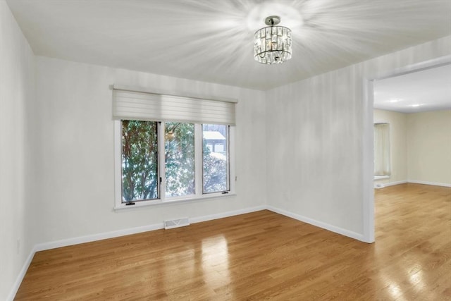 unfurnished room featuring visible vents, a notable chandelier, baseboards, and wood finished floors