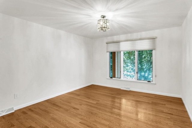 spare room featuring wood finished floors, visible vents, and baseboards