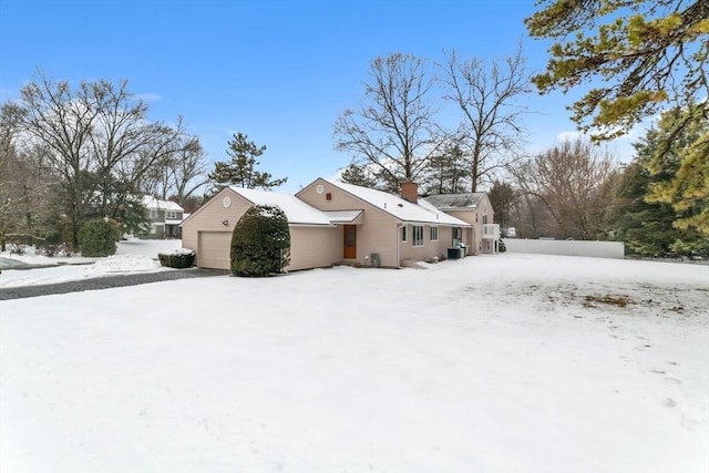 snow covered property featuring a chimney and a detached garage