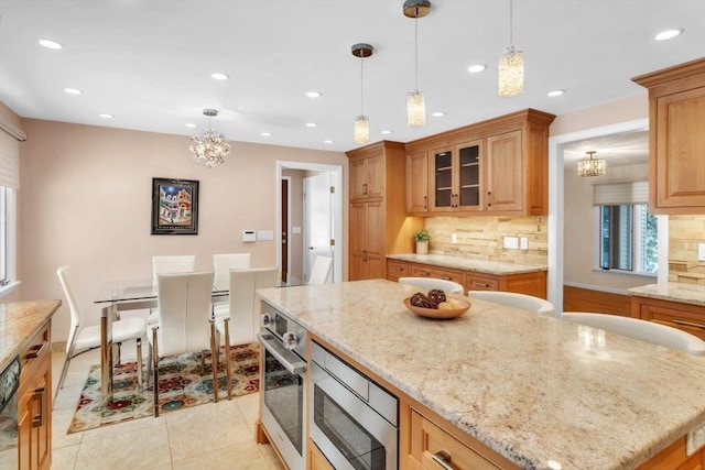 kitchen featuring appliances with stainless steel finishes, light stone countertops, glass insert cabinets, and decorative light fixtures