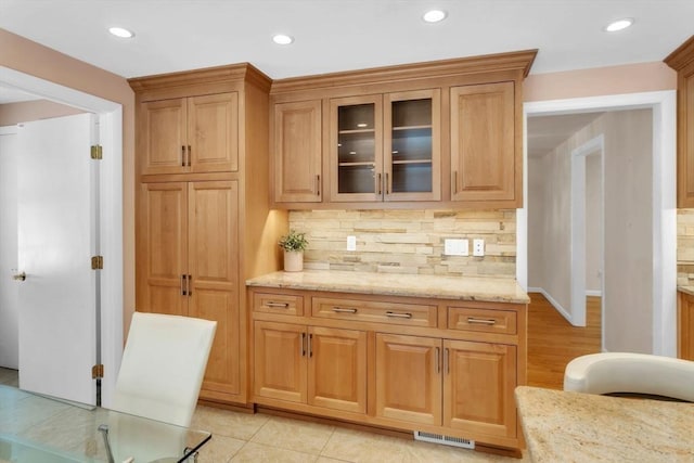 kitchen with glass insert cabinets, decorative backsplash, light stone counters, and recessed lighting