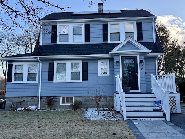 view of front of home featuring roof mounted solar panels, a chimney, and roof with shingles