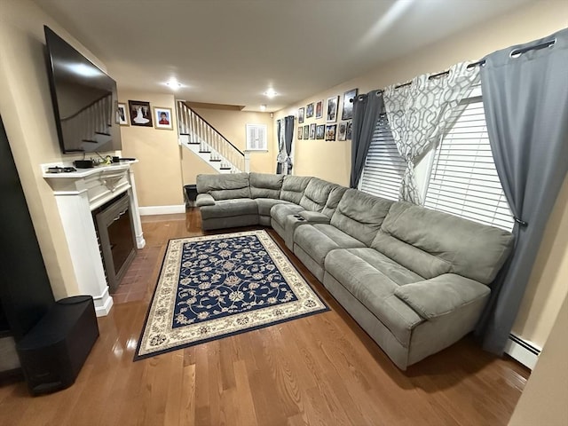 living area featuring a baseboard heating unit, a fireplace, wood finished floors, baseboards, and stairs