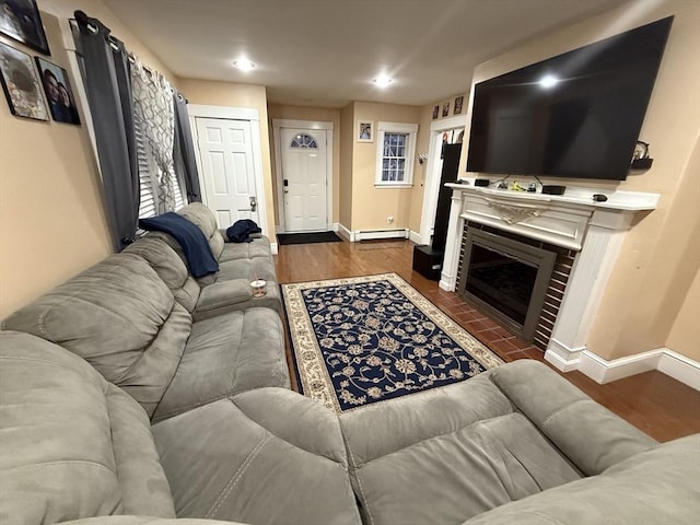 living area featuring recessed lighting, a baseboard heating unit, wood finished floors, baseboards, and a glass covered fireplace