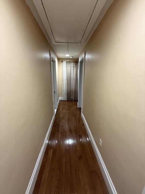 hallway featuring attic access, dark wood finished floors, and baseboards