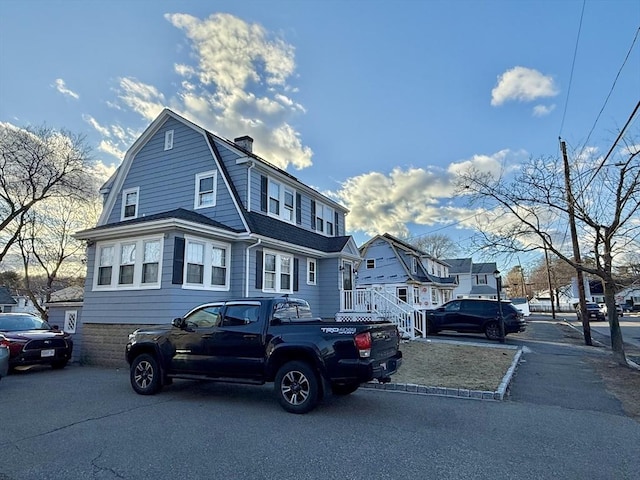 view of front of house featuring a shingled roof, a chimney, a residential view, and a gambrel roof