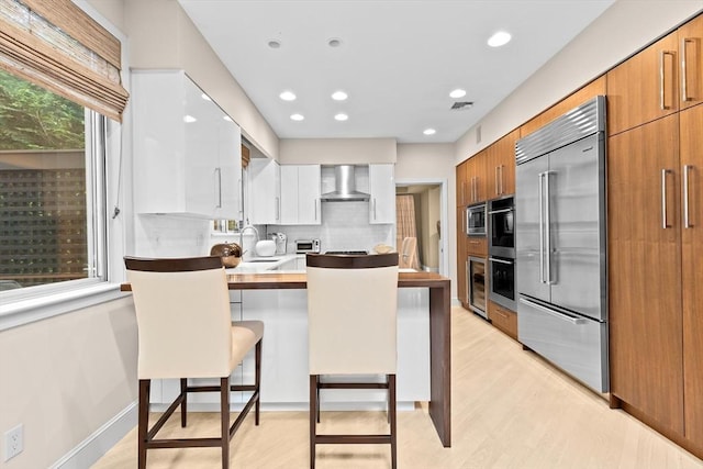 202 Allandale Rd Unit A, Boston, MA 02467 - kitchen featuring built in appliances, wall chimney exhaust hood, a peninsula, tasteful backsplash, and a breakfast bar