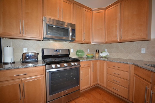 kitchen featuring backsplash, dark stone countertops, and appliances with stainless steel finishes