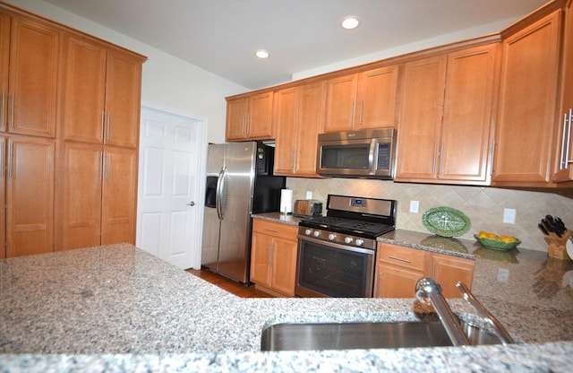 kitchen featuring sink, light stone counters, stainless steel appliances, and tasteful backsplash