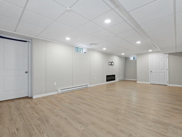 basement with a baseboard radiator, light hardwood / wood-style flooring, and a drop ceiling