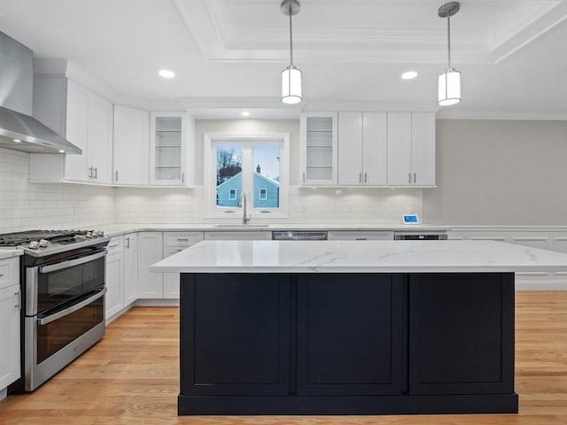 kitchen with light wood-type flooring, wall chimney exhaust hood, stainless steel appliances, a center island, and white cabinetry