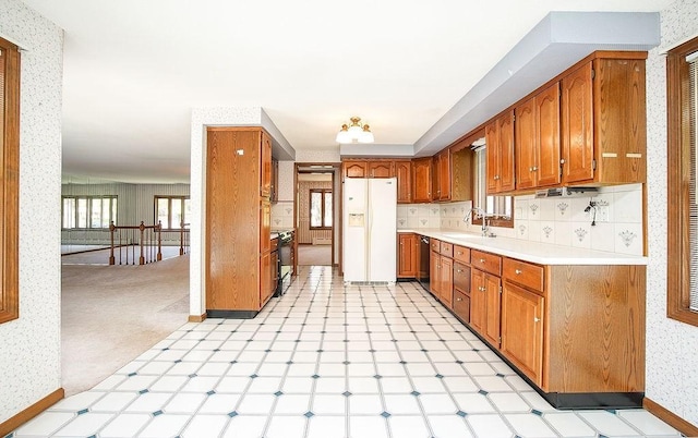 kitchen featuring white refrigerator with ice dispenser, a sink, light countertops, black dishwasher, and wallpapered walls
