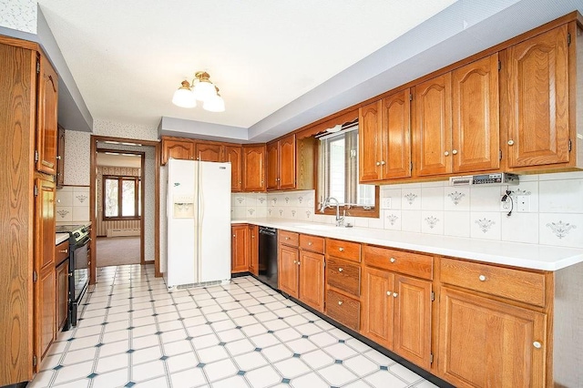 kitchen with a healthy amount of sunlight, brown cabinets, a sink, black appliances, and light floors