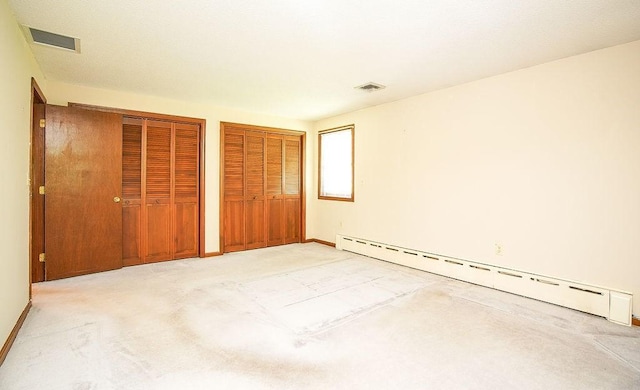 unfurnished bedroom with multiple closets, light carpet, visible vents, and a baseboard radiator