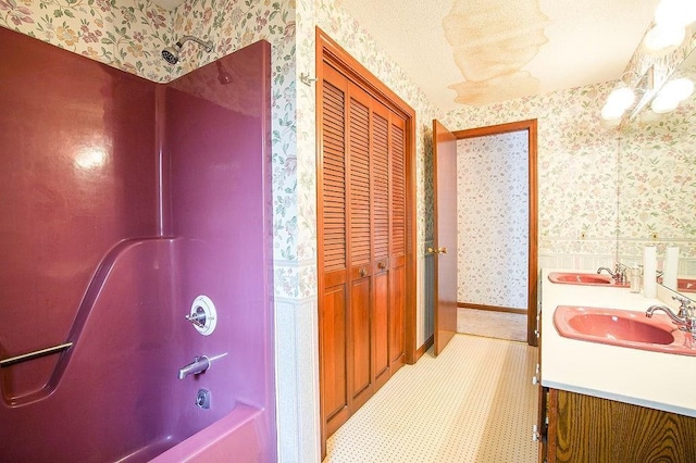 bathroom with double vanity, a sink, bathtub / shower combination, and wallpapered walls