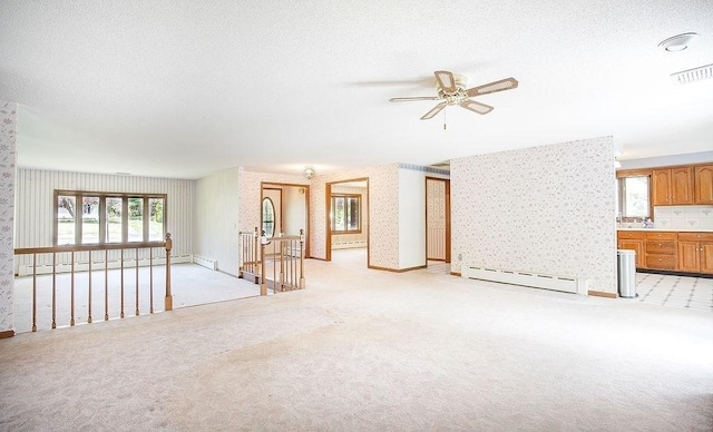 unfurnished living room featuring visible vents, ceiling fan, baseboard heating, and a wealth of natural light