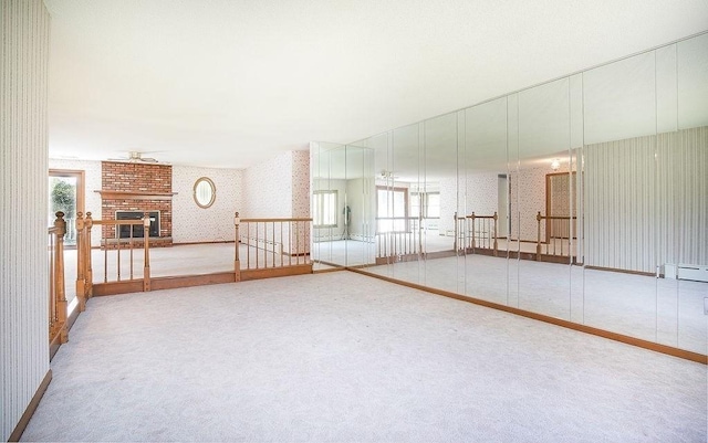 carpeted spare room with a brick fireplace, a ceiling fan, wallpapered walls, and baseboards
