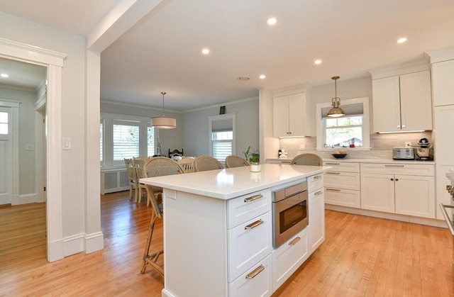 kitchen featuring stainless steel microwave, crown molding, light countertops, and a breakfast bar area