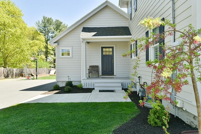property entrance with a shingled roof, a yard, and fence