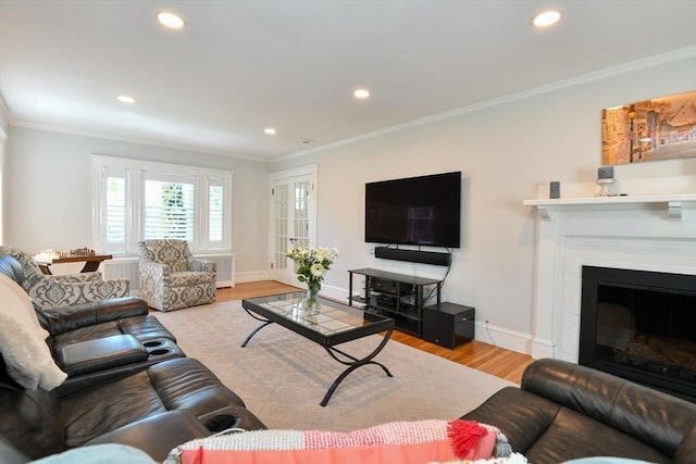 living area with wood finished floors, recessed lighting, crown molding, a brick fireplace, and baseboards