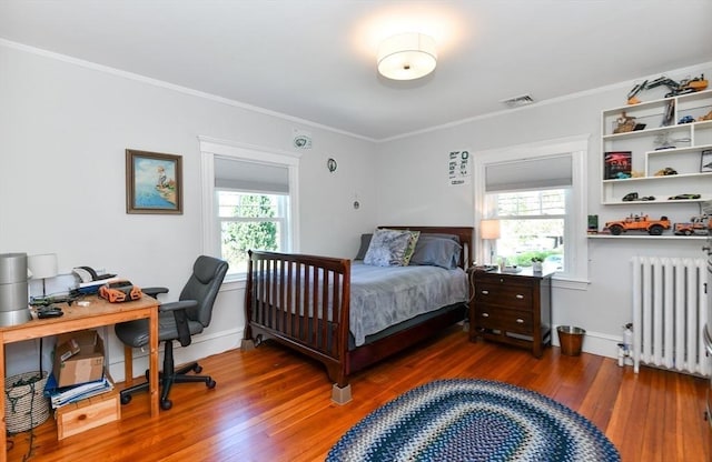 bedroom with ornamental molding, radiator heating unit, visible vents, and wood finished floors