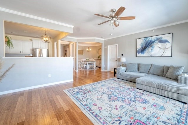 living area with ceiling fan with notable chandelier, ornamental molding, baseboards, and light wood-style floors