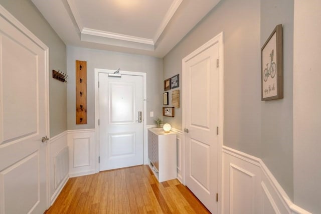 doorway with light wood-style floors, a raised ceiling, wainscoting, and a decorative wall