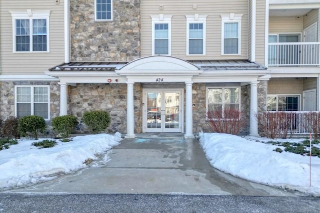 snow covered property entrance with stone siding and french doors