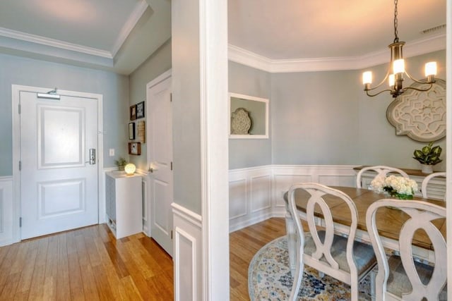 dining space featuring a wainscoted wall, visible vents, light wood-style floors, ornamental molding, and a chandelier