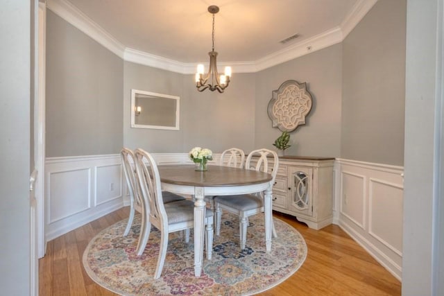 dining room featuring crown molding, light wood finished floors, visible vents, wainscoting, and a chandelier