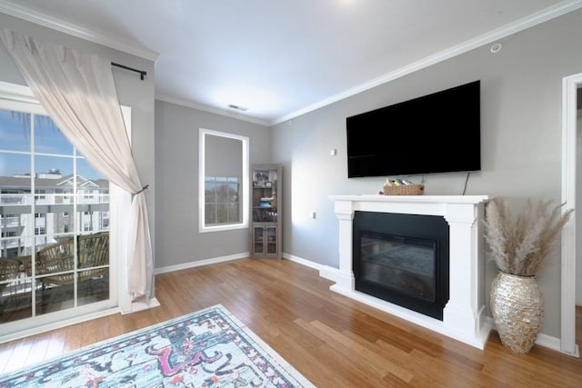 living area featuring baseboards, wood finished floors, a glass covered fireplace, and crown molding