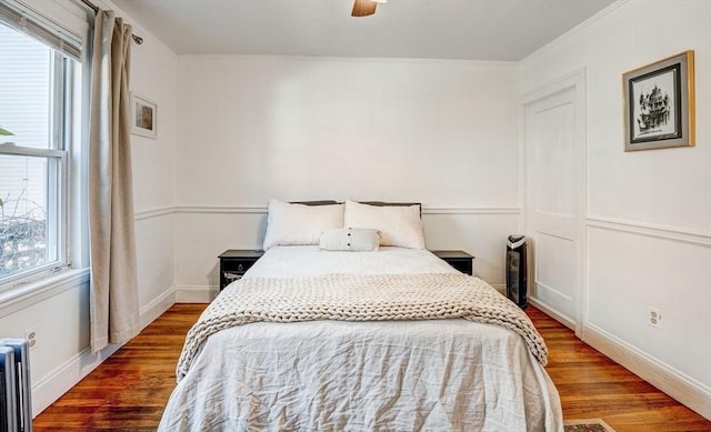 bedroom with crown molding, baseboards, radiator, and wood finished floors