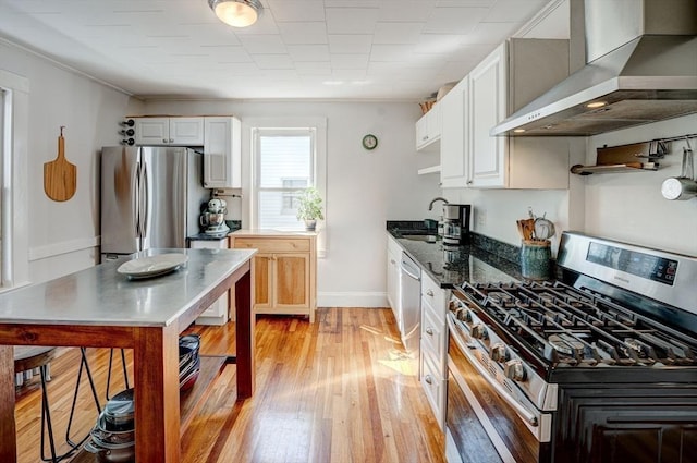 kitchen featuring wall chimney range hood, stainless steel appliances, white cabinetry, and light wood-style flooring