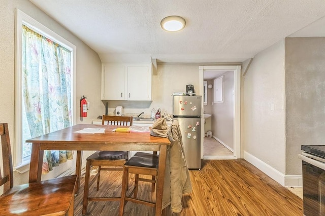dining space featuring light wood-style flooring, a textured ceiling, and baseboards