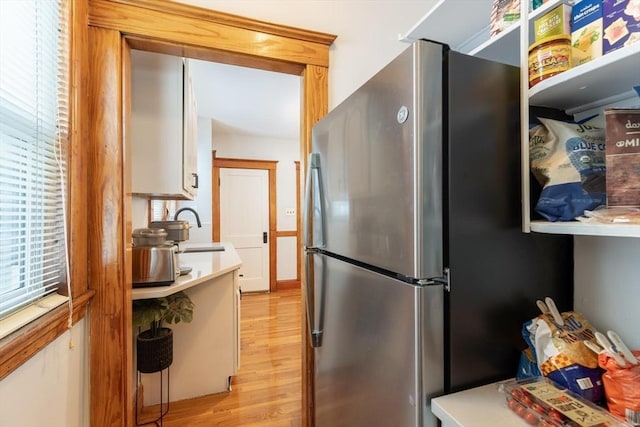 kitchen with sink, white cabinets, light hardwood / wood-style flooring, and stainless steel refrigerator