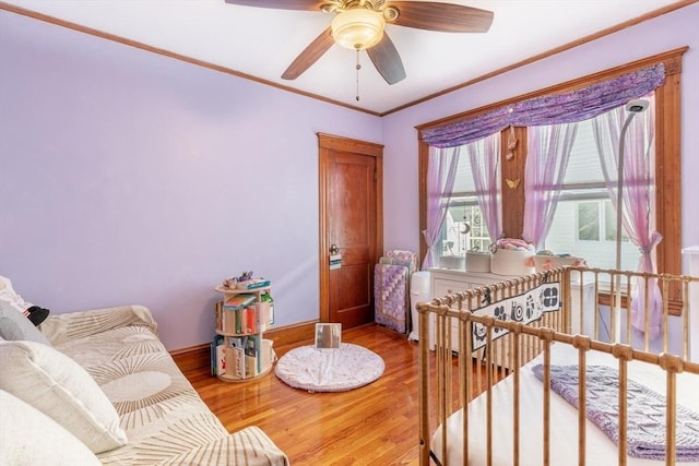 bedroom featuring ceiling fan, a crib, ornamental molding, and hardwood / wood-style flooring