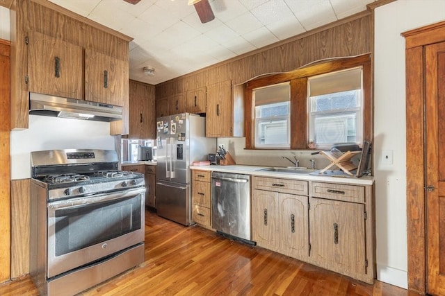 kitchen featuring dark hardwood / wood-style flooring, stainless steel appliances, wooden walls, sink, and ceiling fan