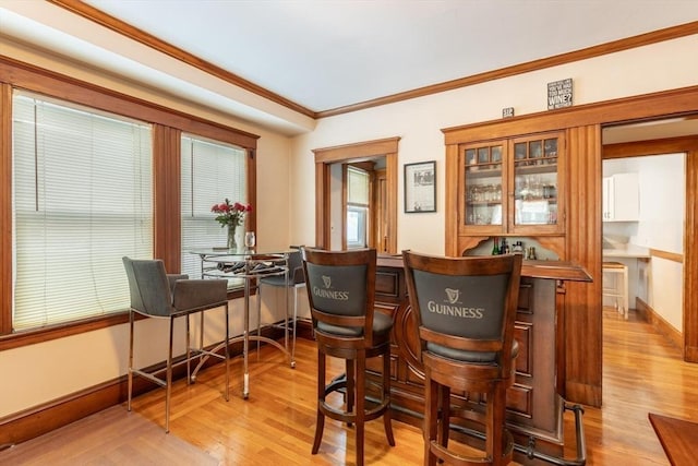 bar with light wood-type flooring and crown molding