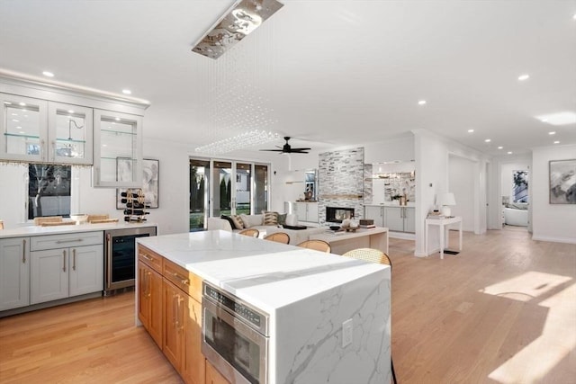 kitchen with light stone counters, ceiling fan, light hardwood / wood-style floors, and wine cooler