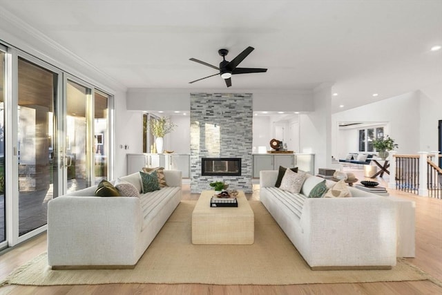 living room featuring crown molding, a stone fireplace, ceiling fan, and light wood-type flooring