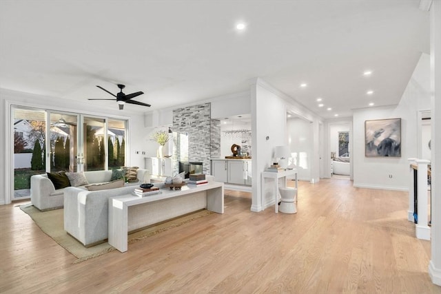 living room featuring ceiling fan, a stone fireplace, crown molding, and light wood-type flooring