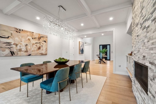 dining space featuring coffered ceiling, a stone fireplace, light hardwood / wood-style flooring, and beamed ceiling